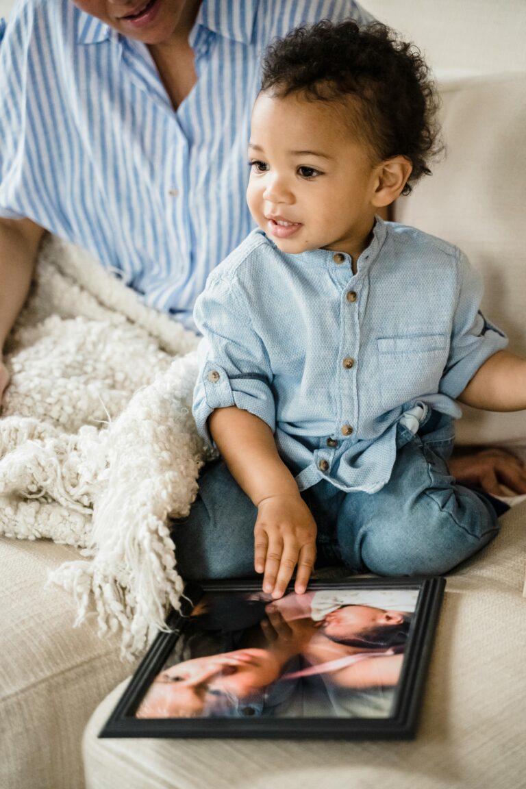 A cute child seated on a couch with an adult, admiring a family photograph. Cozy setting.